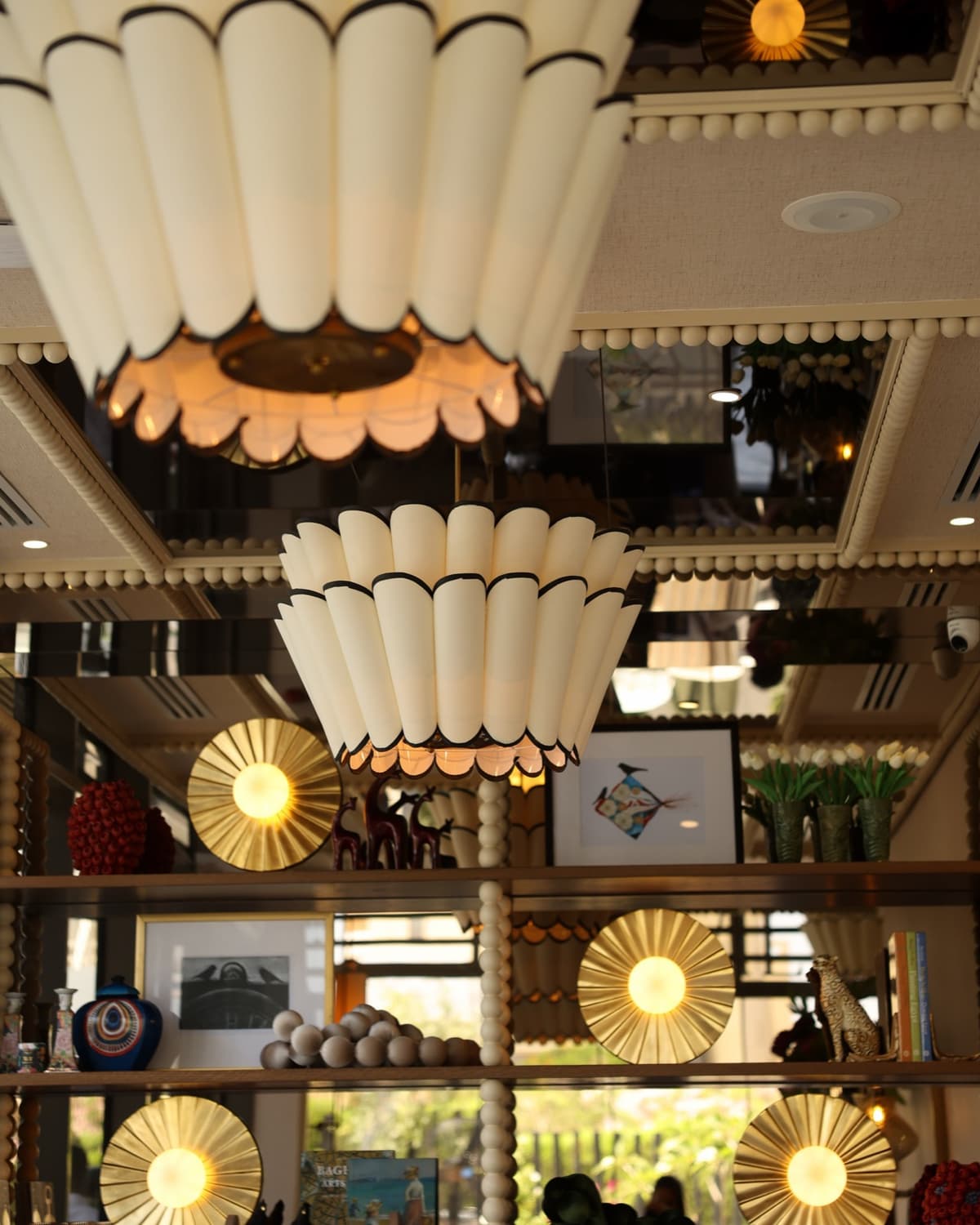 The interior at Willow's Golf Central, with fluted scalloped pendant lights above mirrored shelving displaying sunburst lamps, framed prints and white tulips.