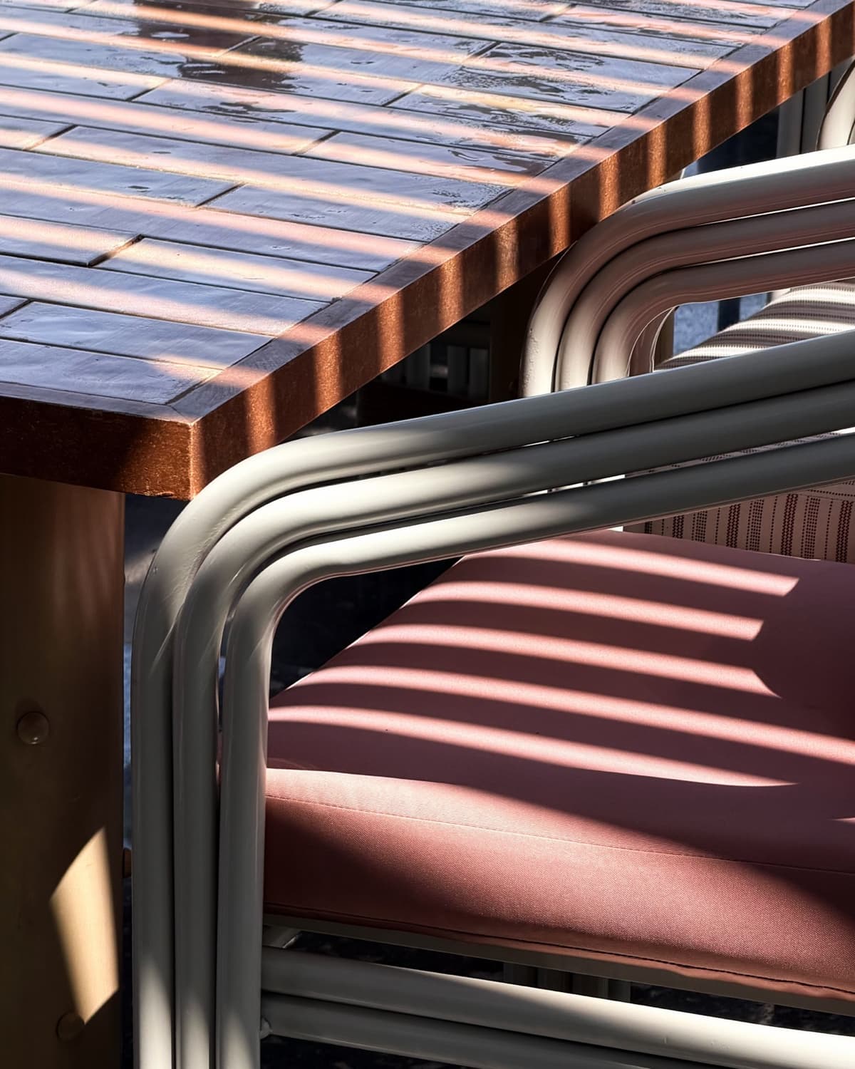 The terrace at Willow's Golf Central, with a rust-edged tiled table and a cream-framed armchair under the raked shadows of a pergola.